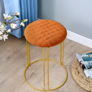 Detailaufnahme des orangefarbenen Samt-Rundhockers mit Goldmetallbeinen im Wohnzimmer.