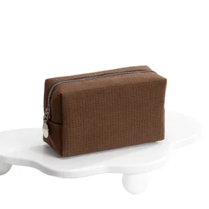 Moderne koffiebruine toilettas met wafelstructuur en rits op een witte standaard