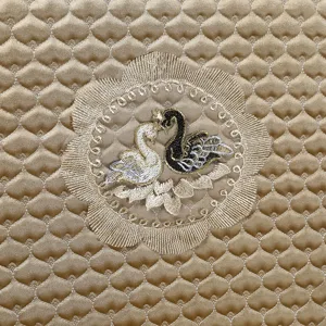 Detailed macro view of golden quilted chair cover with elegant swan embroidery pattern