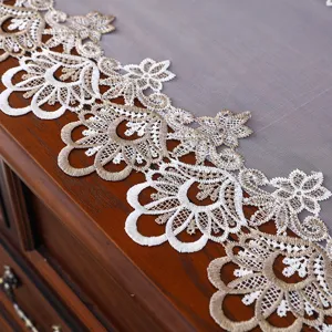 Dettaglio di runner da tavola ricamato in pizzo bianco e oro, elegante decoro europeo.
