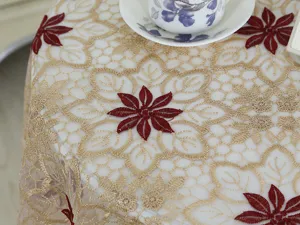 Detalle de mantel bordado de encaje con malla dorada fina y motivo floral rojo.