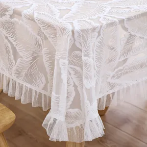 Detalle de mantel de encaje blanco con elegante patron de plumas y borde de volantes.
