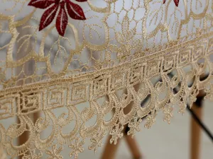 Vista detallada del mantel de encaje dorado bordado con flores rojas y un borde elegante.