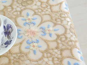 Close-up detail of elegant gold lace embroidery tablecloth with blue floral accents for home decor.