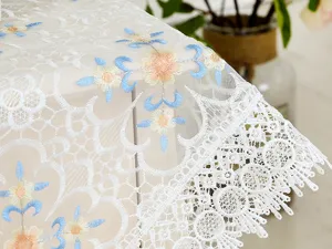 Detailed view of white lace tablecloth with blue yellow floral embroidery, elegant home decor.