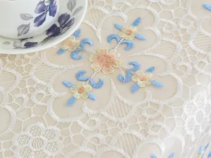 Detailed white lace tablecloth with blue and yellow floral embroidery for elegant home decor.