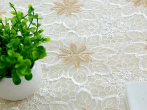 Primer plano de mantel de encaje blanco con bordado floral dorado y textura delicada.