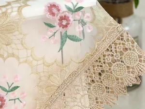 Close-up of exquisite golden lace tablecloth with delicate pink floral embroidery detail.