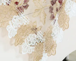 Close-up of delicate lace embroidery tablecloth featuring white, gold and red floral patterns.