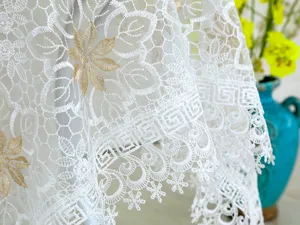 Exquisito detalle de mantel de encaje blanco con elegante diseño de bordado floral dorado.
