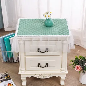Funda acolchada para mesita de noche con ribete de encaje blanco y falda de malla decorativa.