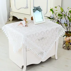 Exquisite white lace embroidery detail on bedside table cover, elegant floral pattern.
