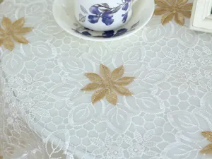 Detalle del mantel de encaje blanco con elegante diseño floral y detalles dorados.