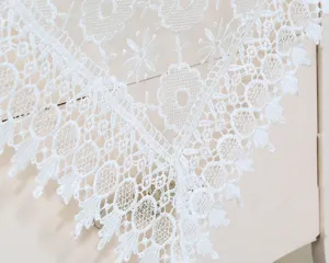White lace embroidered tablecloth detail, elegant floral pattern fabric dust cover for table.