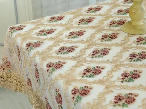Vista detallada del mantel bordado de encaje blanco con motivo floral dorado para el hogar.