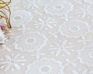 White lace embroidered tablecloth fabric detail shot, elegant floral pattern home decor.