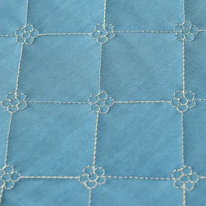 Close-up of blue quilted stool cover fabric with elegant golden embroidered grid and flower patterns.