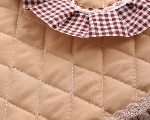 Close-up detail of quilted fabric toilet cover with brown checkered ruffle trim, soft texture.