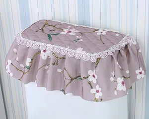 Quilted fabric toilet tank cover with pastoral floral print and elegant white lace trim detail.