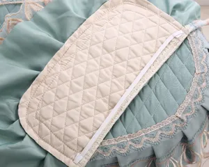 Detail view of quilted fabric toilet seat cover featuring elegant lace trim and soft padding.
