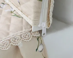 Close up of quilted beige fabric toilet cover detail with delicate white lace trim and zipper.