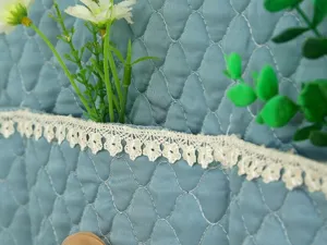 Nahaufnahme der gesteppten Kühlschrank-Staubschutzhülle mit eleganter Spitzenborte, Heimtextil.
