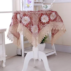 Dettaglio tovaglia tonda bordeaux con ricamo floreale bianco e bordi in pizzo beige
