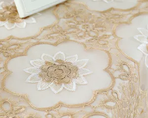 Dettaglio macro di ricamo floreale oro e bianco su elegante tovaglia in filato di vetro