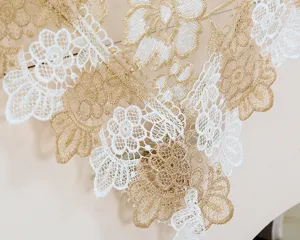 Detailed close-up of exquisite white and gold floral lace embroidery fabric texture.