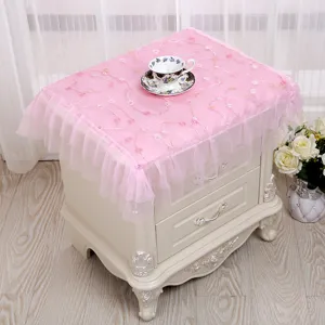 Cubierta de encaje rosa para mesita de noche con bordado floral y volantes en el hogar.