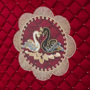 Detailed close-up of red quilted velvet cushion featuring elegant gold lace and swan embroidery.