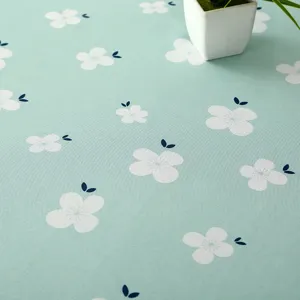 Vue détaillée d'une nappe vert clair imperméable avec motif de fleurs blanches et petite plante.