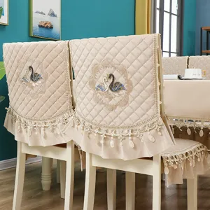 Detail shot of quilted dining chair cover with elegant swan embroidery and lace trim design.