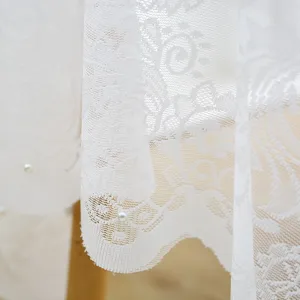 Détail de nappe en dentelle blanche avec broderies élégantes et perles décoratives.