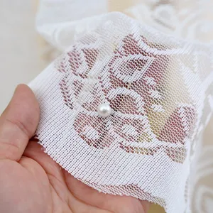Close-up macro detail of white embroidered lace tablecloth with decorative pearl accent.