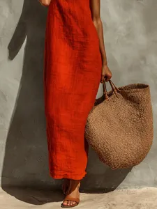 Dettaglio di abito lungo boho rosso, borsa in paglia intrecciata e sandali casual.