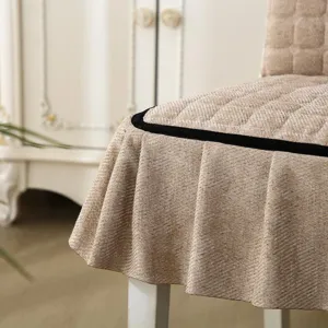 Quilted dining chair cover, beige fabric with black velvet trim and pleated skirt detail.