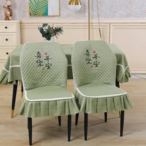 Quilted elastic dining chair cover detail, sage green fabric with embroidered text and ruffles.