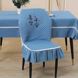 Blue elastic dining chair cover with ruffled skirt and elegant embroidered back design.