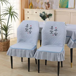 Detailed view of grey quilted dining chair cover with elegant ruffle skirt and embroidery.