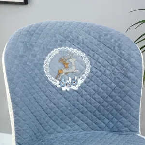 Detailed view of blue quilted dining chair cover featuring elegant embroidered deer and lace.