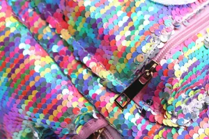Macro detail of colorful rainbow sequins and a smooth pink zipper on a unicorn backpack.