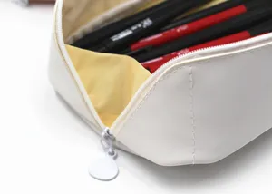 Gros plan d'une trousse en similicuir crème montrant la fermeture éclair et la doublure jaune