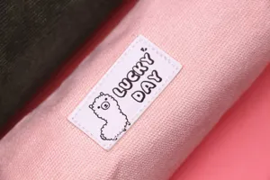 Close-up of pink corduroy pencil case featuring a cute alpaca Lucky Day label detail.