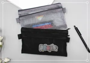 Macro detail of black and grey mesh pencil cases showing dual zippers and cute characters