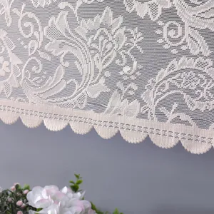 Dettaglio di una elegante tenda in pizzo bianco con motivi floreali e bordi a conchiglia.