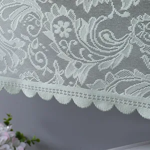 Dettaglio della copertura antipolvere in pizzo bianco con motivi floreali e bordo a festone.