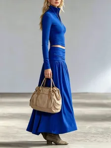 Side view of a model wearing a royal blue zip-up top and low-waist pleated maxi skirt