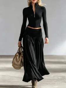 Model wearing black long-sleeve zip-up top and low-waisted maxi skirt set with handbag