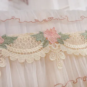 Primo piano di eleganti ricami floreali rosa e pizzo su una copertura in rete per condizionatore.